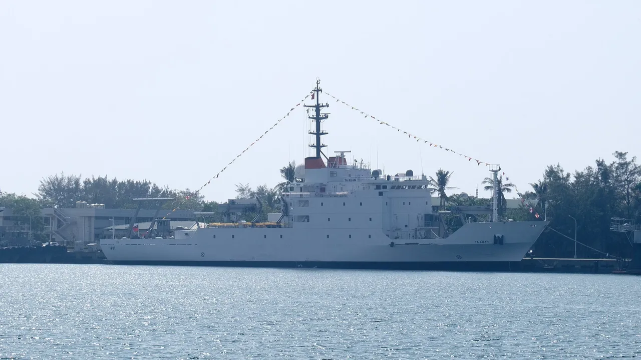 A large white naval survey ship decorated with signal flags lies moored at a harbour pier under a hazy sky